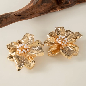 Close-up of golden floral earrings with white pearls and textured hammer pattern finish