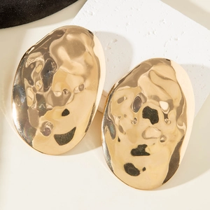 Close-up of golden irregular wavy stud earrings with hammered metal texture and glossy finish