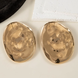 Detailed view of large gold-tone irregular earrings with hammer textured wavy surface