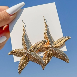 Golden starfish dangle earrings with textured finish against a clear blue sky background