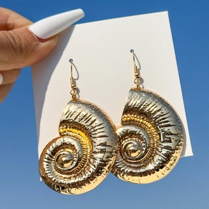 Golden nautilus shell spiral earrings with dot texture against a blue sky background