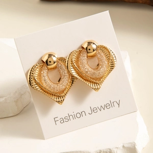Macro view of gold heart earrings with radiant grooves and woven texture on a card