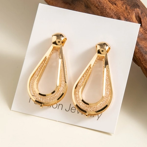 Detail of gold geometric drop earrings with woven mesh texture on display card