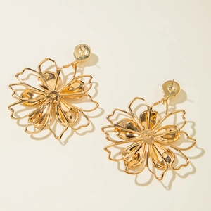 Macro detail of golden hollow flower earrings with metallic luster on cream background