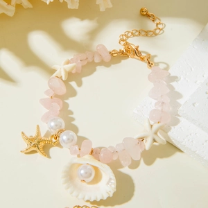 Détail d'un bracelet en perles avec coquillages, pierres roses et pendentif étoile de mer