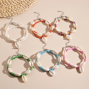 Détail de six bracelets de cheville bohème avec perles colorées et coquillages sur fond beige