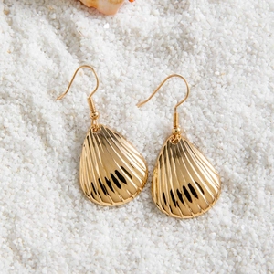 Détail des boucles d'oreilles bohèmes en coquillage doré sur fond de sable blanc de plage