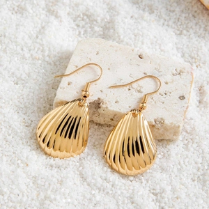 Détail de boucles d'oreilles coquillage dorées avec rayures verticales sur pierre blanche