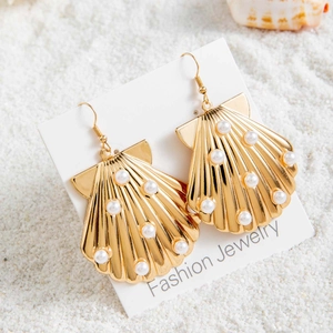 Détail de boucles d'oreilles bohèmes en forme de coquillage doré avec perles blanches