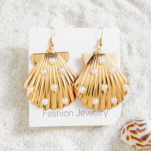Détail de boucles d'oreilles coquillage dorées avec perles blanches sur fond de sable