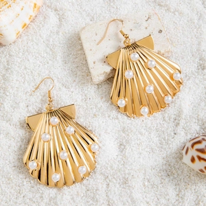 Boucles d'oreilles coquillages dorées avec perles sur sable blanc et conques