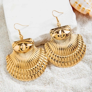 Gros plan de boucles d'oreilles festonnées dorées sur sable blanc pour style marin