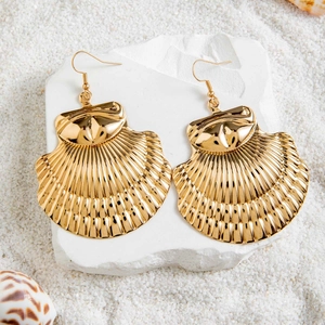Détail de boucles d'oreilles festonnées en or avec perles sur fond de sable blanc fin