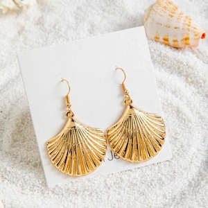 Détail de boucles d'oreilles bohèmes en forme de coquillage doré sur fond de plage de sable