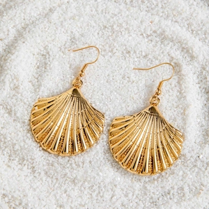 Boucles d'oreilles bohèmes en forme de coquillage doré sur un fond de sable fin