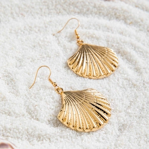 Gros plan de boucles d'oreilles coquillage dorées avec nacre sur fond de sable blanc