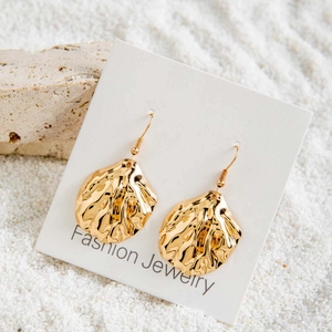 Gros plan de boucles d'oreilles festonnées dorées avec perles sur fond de sable blanc