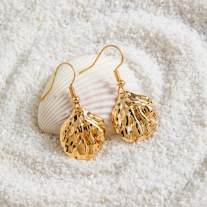 Boucles d'oreilles coquillages dorés bohèmes avec perles sur sable blanc