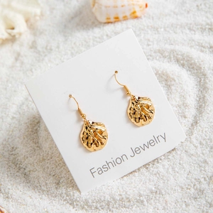 Détails de boucles d'oreilles coquillage dorées sur du sable blanc avec coquilles