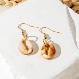 Detail of seashell drop earrings on a white stone surface for a summer beach look