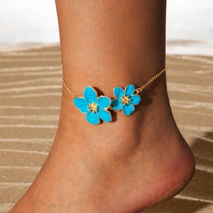 Detail of blue flower anklet with gold chain on sandy beach background with natural shadows
