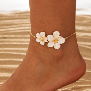 Close-up of golden anklet with two white flower charms on a sandy beach
