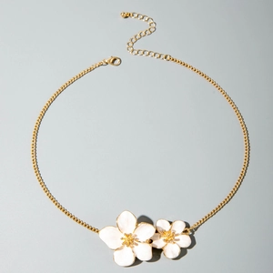 Detail of gold chain necklace featuring two white enamel flower charms with floral accents