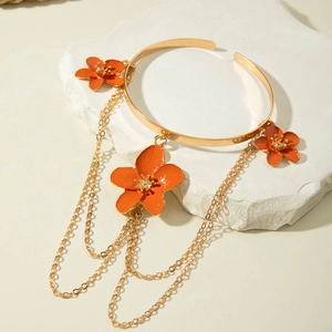 Detail of gold arm cuff with orange enamel flowers and hanging metal tassel chains