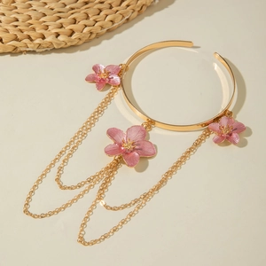 Detail view of a gold bangle featuring pink cherry blossoms and delicate layered chain tassels