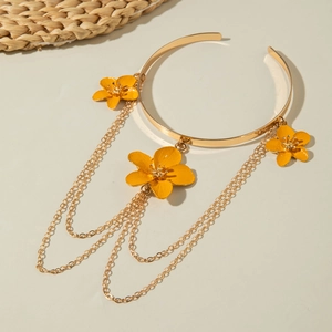 Detail of a gold arm cuff with three yellow flowers and long tassels on a beige background