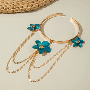 Detailed shot of golden arm cuff featuring blue flowers and layered chain tassels