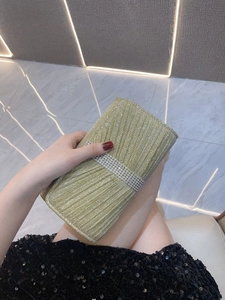 Detail of the golden pleated clutch bag featuring a vertical texture and rhinestone band
