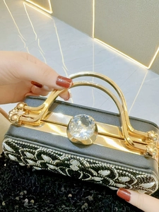 Detailed view of black evening clutch bag with pearl sunflower patterns and large crystal
