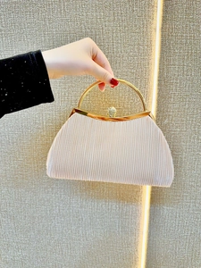 Dettaglio della pochette da sera a pieghe champagne con manico dorato e chiusura diamante