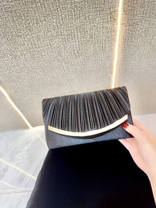 Detail view of the black pleated silk clutch with an elegant gold curved metal trim