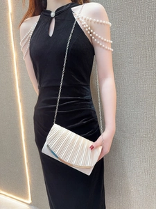 Elegant off-white pleated evening clutch bag with gold metal trim worn on fine chain strap