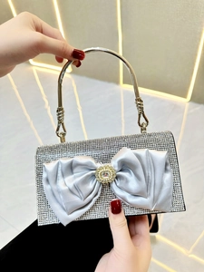 Detailed view of silver rhinestone handbag featuring a large satin bow and metal handle