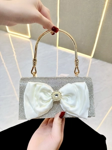 Close-up of silver rhinestone clutch with a large white satin bow and metal ring handle