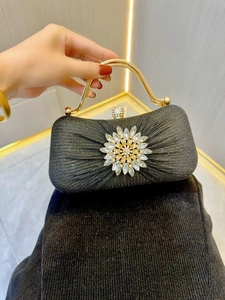 Close-up of black evening clutch bag with crystal flower and gold circular handle