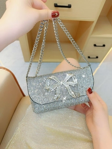 Silver evening clutch bag featuring a large 3D rhinestone bow and metal chain strap