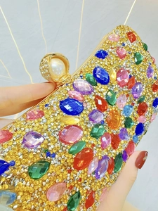 Detail of luxury gold clutch with colorful gemstones and shell pearl clasp held in hand
