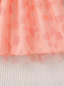 Detailed close-up of coral pink tulle layers with delicate heart-shaped applique texture