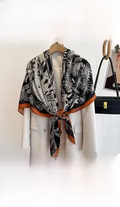 Detail view of large silk scarf featuring black and white palm patterns with orange trim