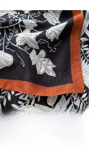 Close-up of black floral silk scarf with white leaf patterns and orange border edges