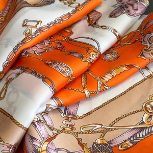 Close-up of luxury silk scarf showing chain print and smooth texture in orange and white