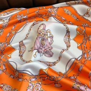 Detail of silk scarf showing vibrant orange horse saddle print and metallic chain patterns