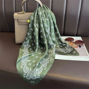 Foulard en soie vert à motif paisley et papillons noué sur un sac à main beige