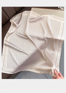 Dettaglio della stampa paisley su foulard di raso beige adagiato su un divano in pelle