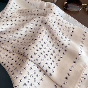 Dettaglio ravvicinato di un foulard di seta rosa con motivo paisley e occhiali da sole