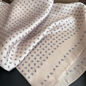 Dettaglio di un foulard in raso beige con motivo paisley e trama setosa premium